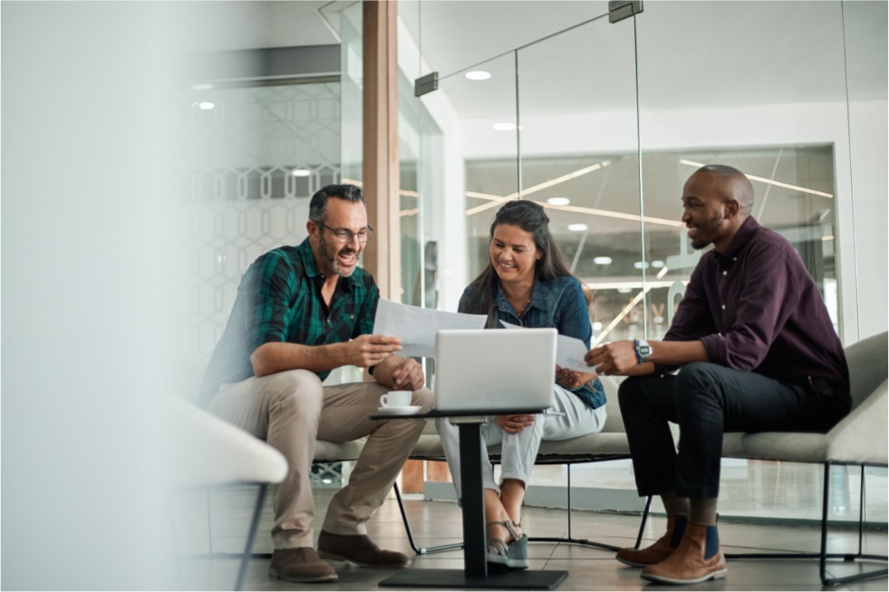 Three coworkers siting around a small table looking at a affiliate benefits with Panorama on a laptop