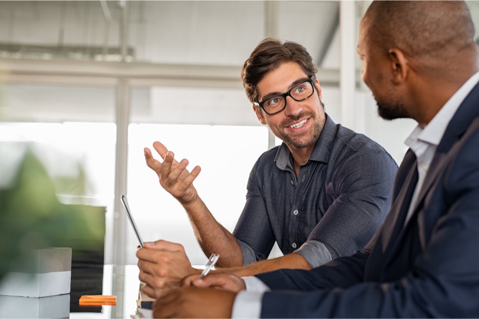 Two male coworkers talking to each other at a glass table